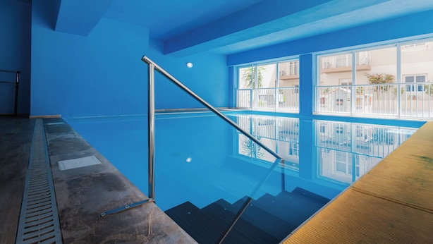 Una piscina interior con paredes de vidrio transparente, una barandilla metálica y vistas al exterior a través de amplias ventanas.