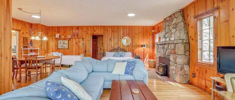 A cozy cabin with a stone fireplace, a large L-shaped sofa, a dining table, and a television.