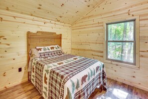 A wooden cabin bedroom with a bed, a window, and a headboard with a bear design.