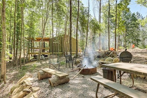 A rustic outdoor setting with a wooden structure, picnic tables, and a campfire. - Gateway to Ouachita National Forest! Cozy Cabin (Glenwood)