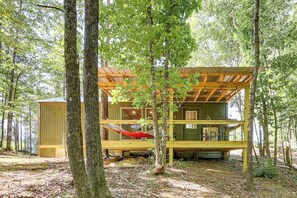 A wooden cabin with a porch, a hammock, and a small shed in a forest.