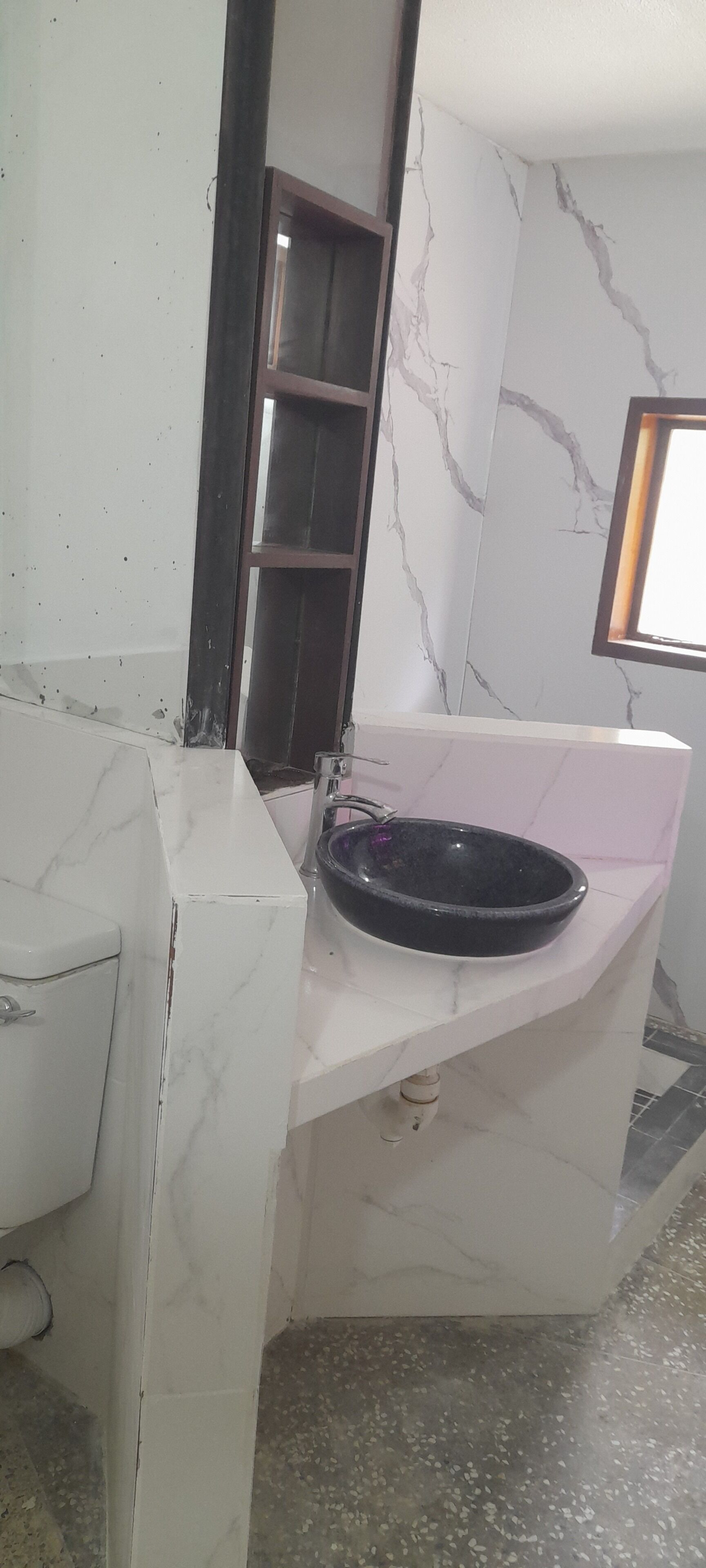 A bathroom with a marble sink, a mirror, and a window.