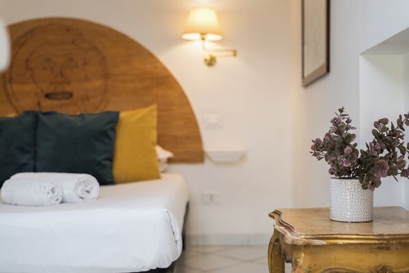 A neatly made bed with pillows, a wall-mounted light fixture, and a small table with a plant. - Cozy 1-bedroom Loft in gorgeous Roma Trastevere with AC (Roma)