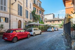 A cobblestone street lined with historic buildings, parked cars, and a café with outdoor seating. - Cozy 1-bedroom Loft in gorgeous Roma Trastevere with AC (Roma)