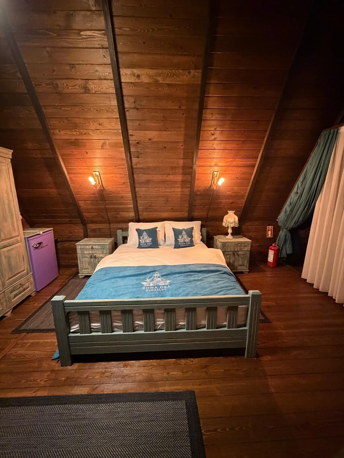 A wooden ceiling with a bed centered in a room, flanked by nightstands and a dresser.