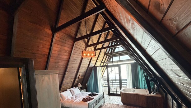 Un dormitorio con techo inclinado, una cama, un aparador, una ventana y un baño con bañera.