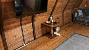 Una habitación con una televisión montada en una pared de madera, una mesita de madera con una tetera y una taza, un sofá y una alfombra con estampado en espiga.