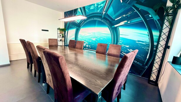 Ein Konferenzraum mit großem Tisch, sechs Stühlen und einem futuristischen Wandgemälde.