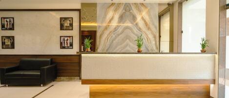 A reception area with a marble wall, a reception desk, a black leather sofa, and framed artwork on the wall.