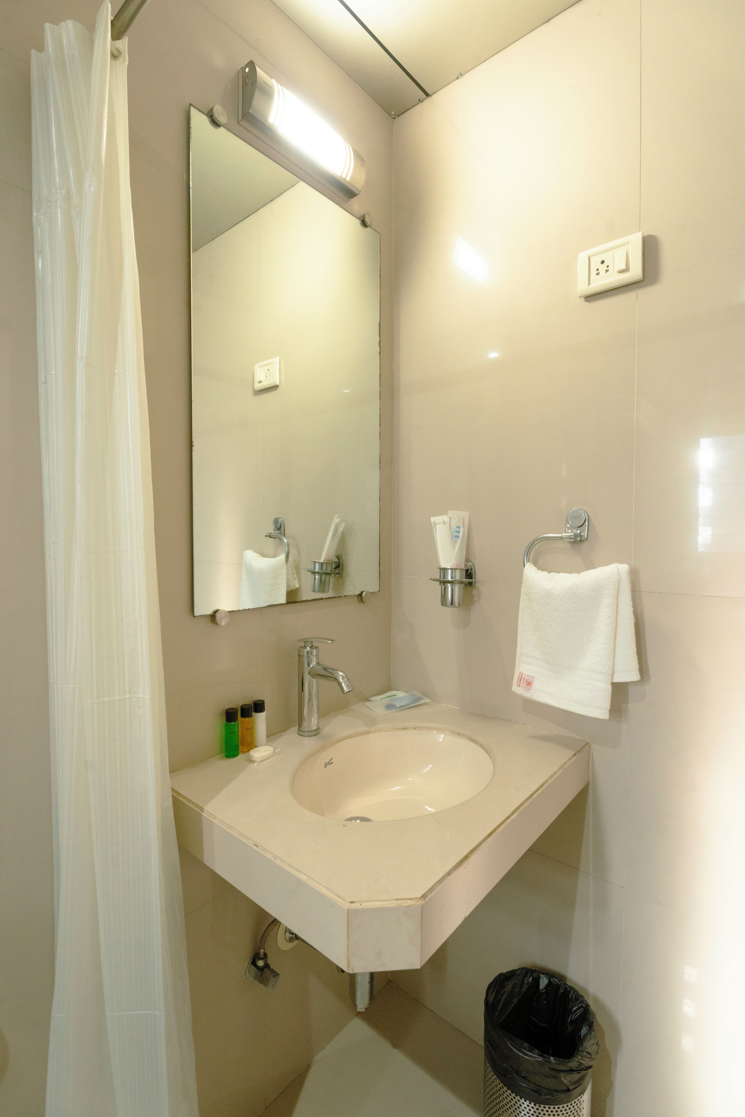 Un baño con lavamanos, espejo, toallero y un cubo de basura.