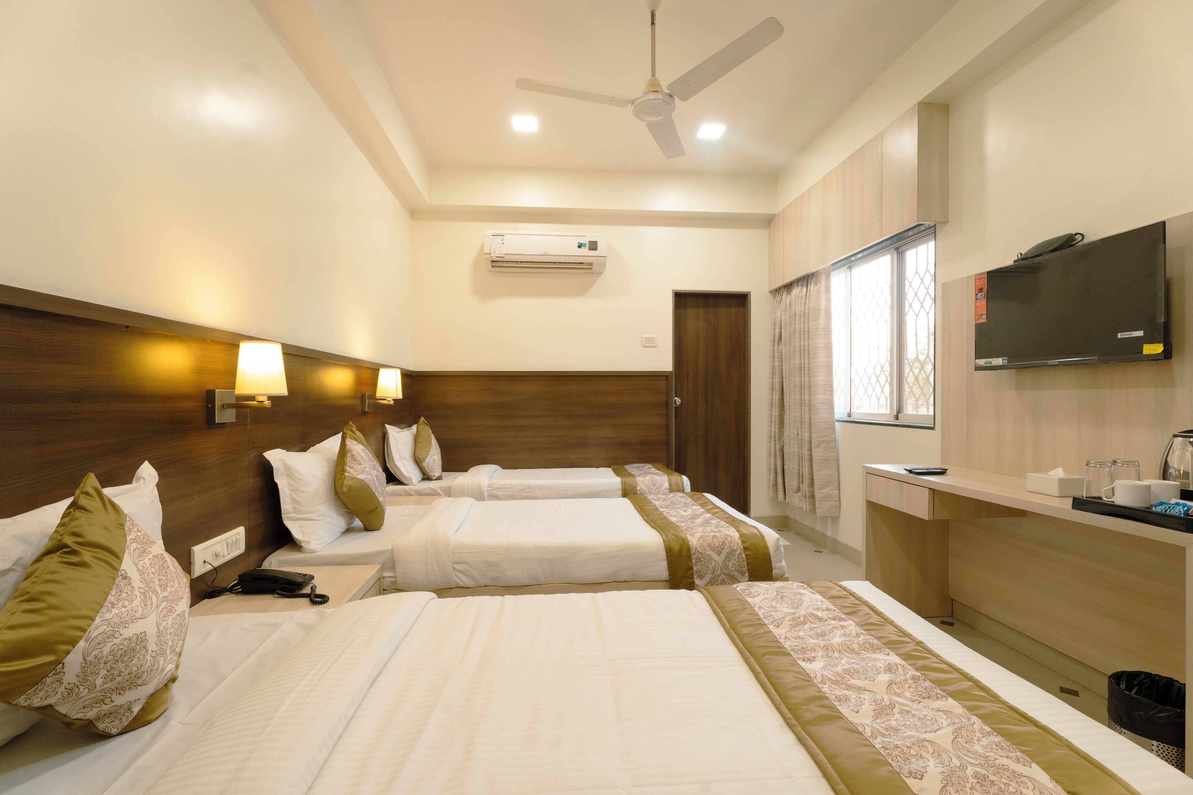 A hotel room with two beds, a TV, a desk, and an air conditioning unit.