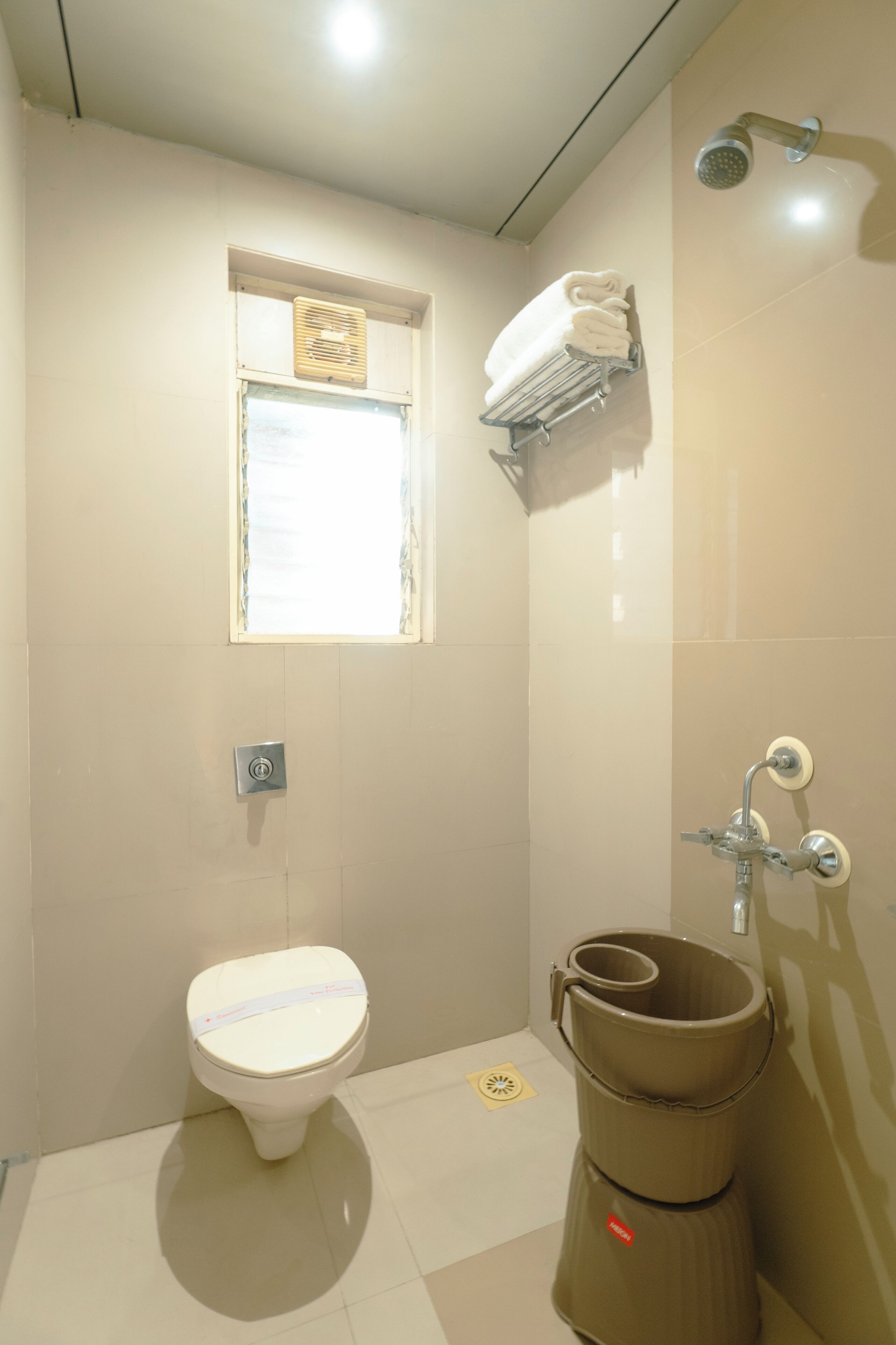 Un baño con inodoro, ventana, toallero, ducha y cubo de basura.