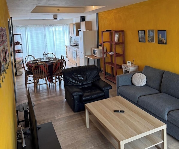 Un espacio habitable compacto con zona de comedor, un sofá, una mesa de centro y un televisor.