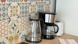 Een keuken met een zwart inductiefornuis, een koffiezetapparaat, een broodrooster en een pan op het aanrecht.