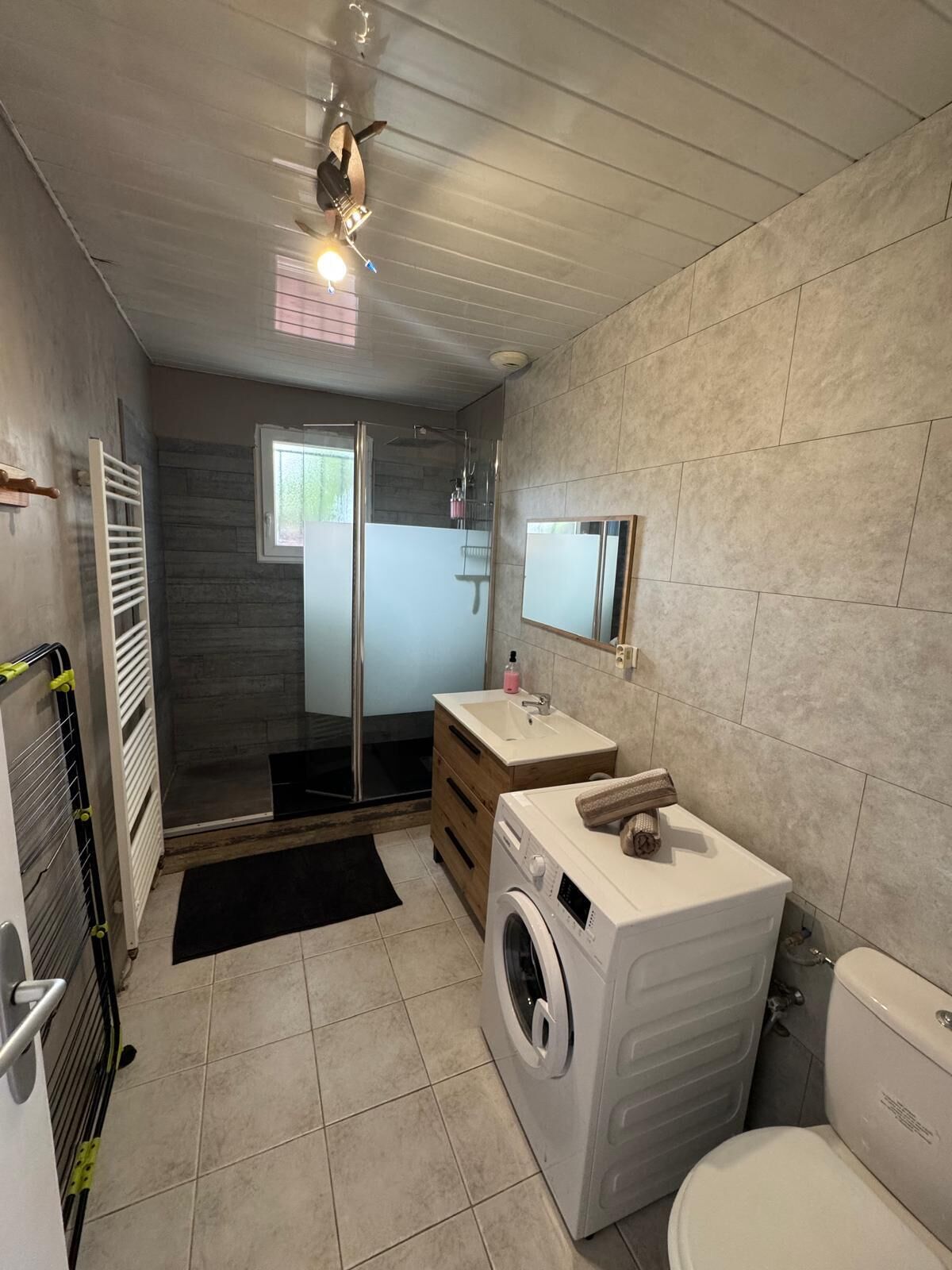 A modern bathroom with a shower, a sink, a washing machine, and a toilet.