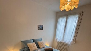 Een slaapkamer met een bed, nachtkastje, lamp en raam met gordijnen.