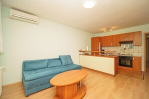 A compact living space with a sofa, a small wooden table, a kitchenette, and a ceiling light. - Vacation apartment for 4 people with balcony and private parking space (Crikvenica)