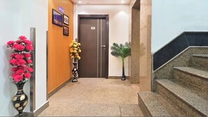 A hotel lobby with a wooden panel wall, a reception desk, a staircase, and a door marked 'Lobby'. - Oly Emporio Near NDLS (New Delhi)