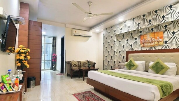 A hotel room with a bed, a sofa, a TV, a ceiling fan, and a patterned wall. - Oly Emporio Near NDLS (New Delhi)