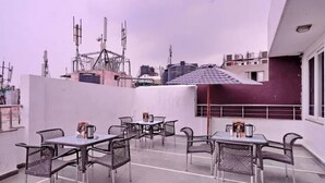 A rooftop terrace with outdoor seating, a checkered umbrella, and a cityscape view. - Oly Emporio Near NDLS (New Delhi)
