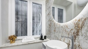 Un baño con un lavamanos blanco, una pared de mármol curvada y una ventana con vidrio esmerilado.