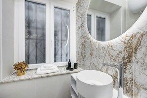 Ein Badezimmer mit einem weißen Waschbecken, einer gewölbten Marmorwand und einem Fenster mit satiniertem Glas.