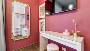 Una habitación con pared rosa, tocador blanco con espejo, televisor de pantalla plana y una pequeña planta en maceta.