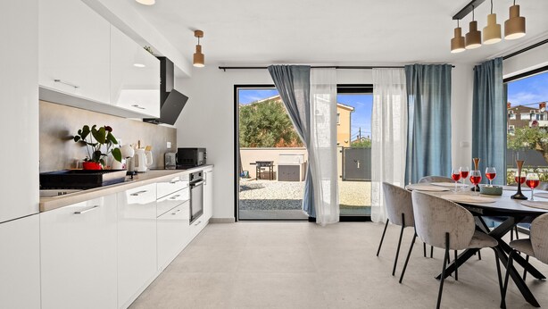 Une cuisine moderne avec des meubles blancs, un coin repas comprenant une table et des chaises, et une porte-fenêtre coulissante donnant sur un espace extérieur.