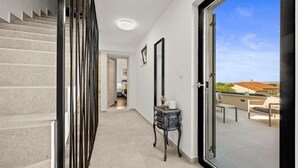 Un couloir avec un escalier, une petite table sur laquelle est posé un vase, et une vue sur un espace patio extérieur.