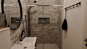 Een badkamer met een bakstenen muur, een grote spiegel, een wastafel, een douche en een kapstok.
