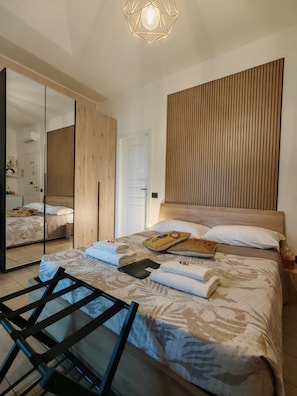 A modern bedroom with a bed, a wooden headboard, a mirror, and a ceiling light fixture. - 3) Double room with private bathroom 8 minutes from Milan Malpensa Airport. (Gallarate)