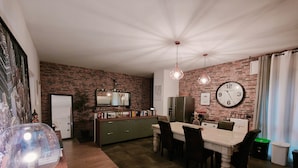 Een eetgedeelte met een bakstenen muur, een klok en een moderne keuken op de achtergrond.