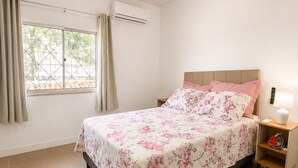 Une chambre à coucher comprenant un lit, des rideaux, un appareil de climatisation, une table de chevet avec une lampe et un téléphone fixé au mur.