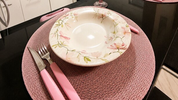 Une cuisine moderne avec des meubles blancs, un plan de travail noir et des sets de table roses.