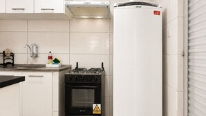 Une cuisine avec des meubles blancs, une cuisinière noire, un réfrigérateur blanc et un dosseret carrelé.