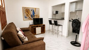 Un salon avec un canapé, un téléviseur et des œuvres d’art ; une cuisine avec un coin repas ; et un escalier.