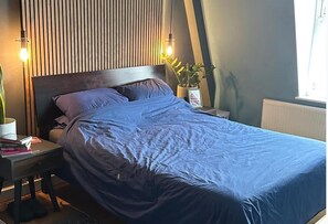 Ein Schlafzimmer mit einem Bett, Nachttischen, einer Zimmerpflanze und einem Fenster.