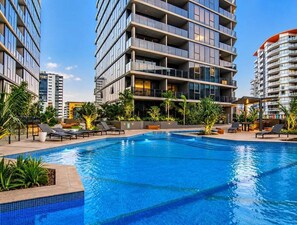 A swimming pool with lounge chairs and a modern building with balconies. - High-Rise Retreat Near South Bank (Brisbane)