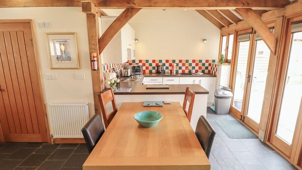 A kitchen with a wooden table, chairs, a tiled backsplash, and a window. - 3b Hideaways (Hunstanton)
