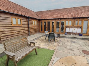 A wooden building with a tiled roof, a patio with a table and chairs, and a bench. - 3b Hideaways (Hunstanton)