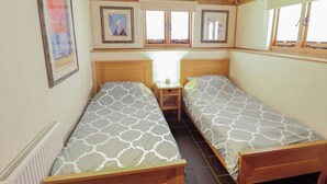 A room with two single beds, a small bedside table, a radiator, and framed artwork on the walls. - 3b Hideaways (Hunstanton)