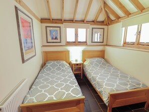 A room with two single beds, a small bedside table, a radiator, and framed artwork on the walls. - 3b Hideaways (Hunstanton)