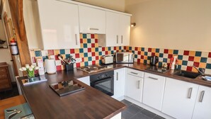 A modern kitchen with white cabinets, a wooden countertop, a microwave, and a tiled backsplash. - 3b Hideaways (Hunstanton)