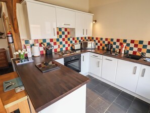 Eine moderne Küche mit weißen Schränken, einer Holzausziehtheke, einer Mikrowelle und einer gefliesten Spritzschutzwand.