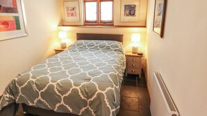 Une chambre à coucher avec un lit, deux tables de chevet avec des lampes, une fenêtre et un radiateur.