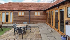 A wooden building with a tiled roof, a patio with a table and chairs, and a blue planter. - 3b Hideaways (Hunstanton)