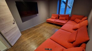 A modern living room with a large sectional sofa, a flat-screen TV mounted on the wall, and a wooden floor. - The Forests Cottage for 10 Guests, Near Center Parcs Trois Forêts (Cirey-sur-Vezouze)