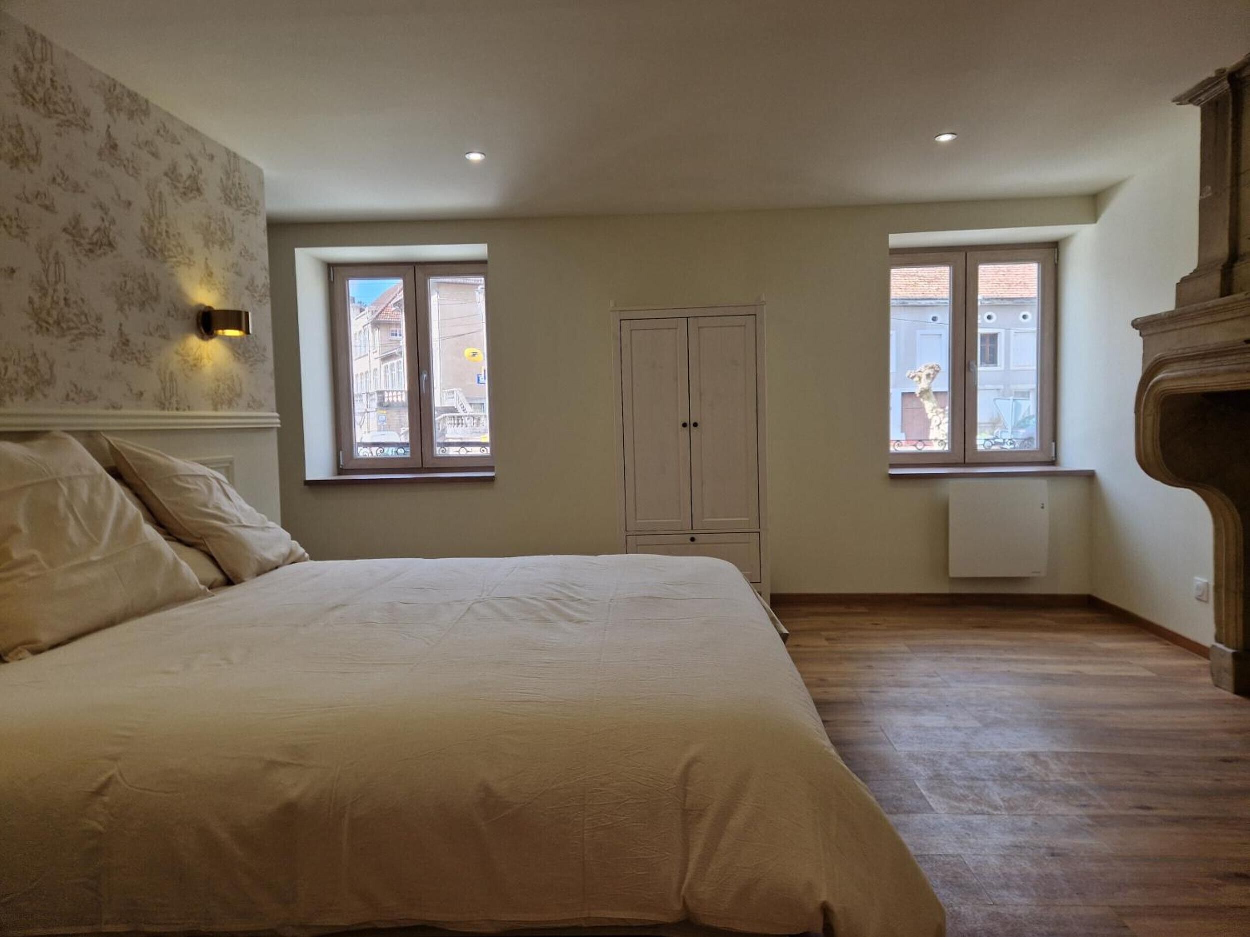 Ein Schlafzimmer mit einem Bett, zwei Fenstern, einem Kleiderschrank und einer Heizung.