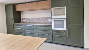 A modern kitchen with green cabinets, a wooden countertop, and a built-in oven. - The Forests Cottage for 10 Guests, Near Center Parcs Trois Forêts (Cirey-sur-Vezouze)