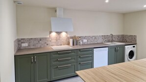 A modern kitchen with a built-in dishwasher, a sink, and a wooden dining table. - The Forests Cottage for 10 Guests, Near Center Parcs Trois Forêts (Cirey-sur-Vezouze)